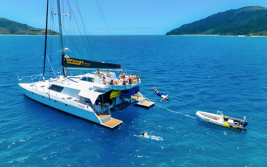 Tourists enjoying a catamaran tour in the Whitsundays, with one diving into the sea.