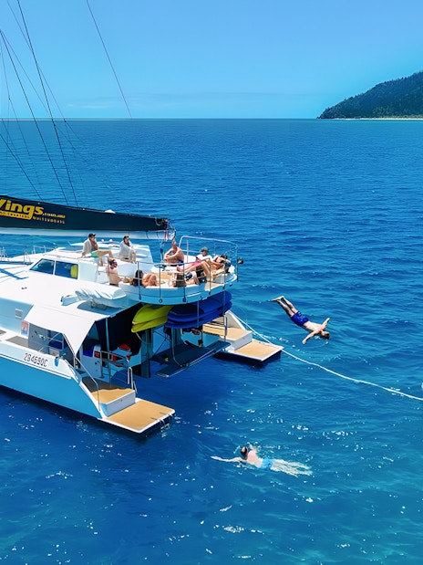 Tourists enjoying a catamaran tour in the Whitsundays, with one diving into the sea.