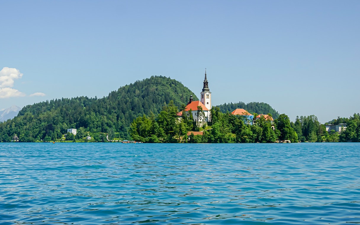 Church of the Assumption of Mary on Bled Lake, Slovenia, surrounded by water and trees.