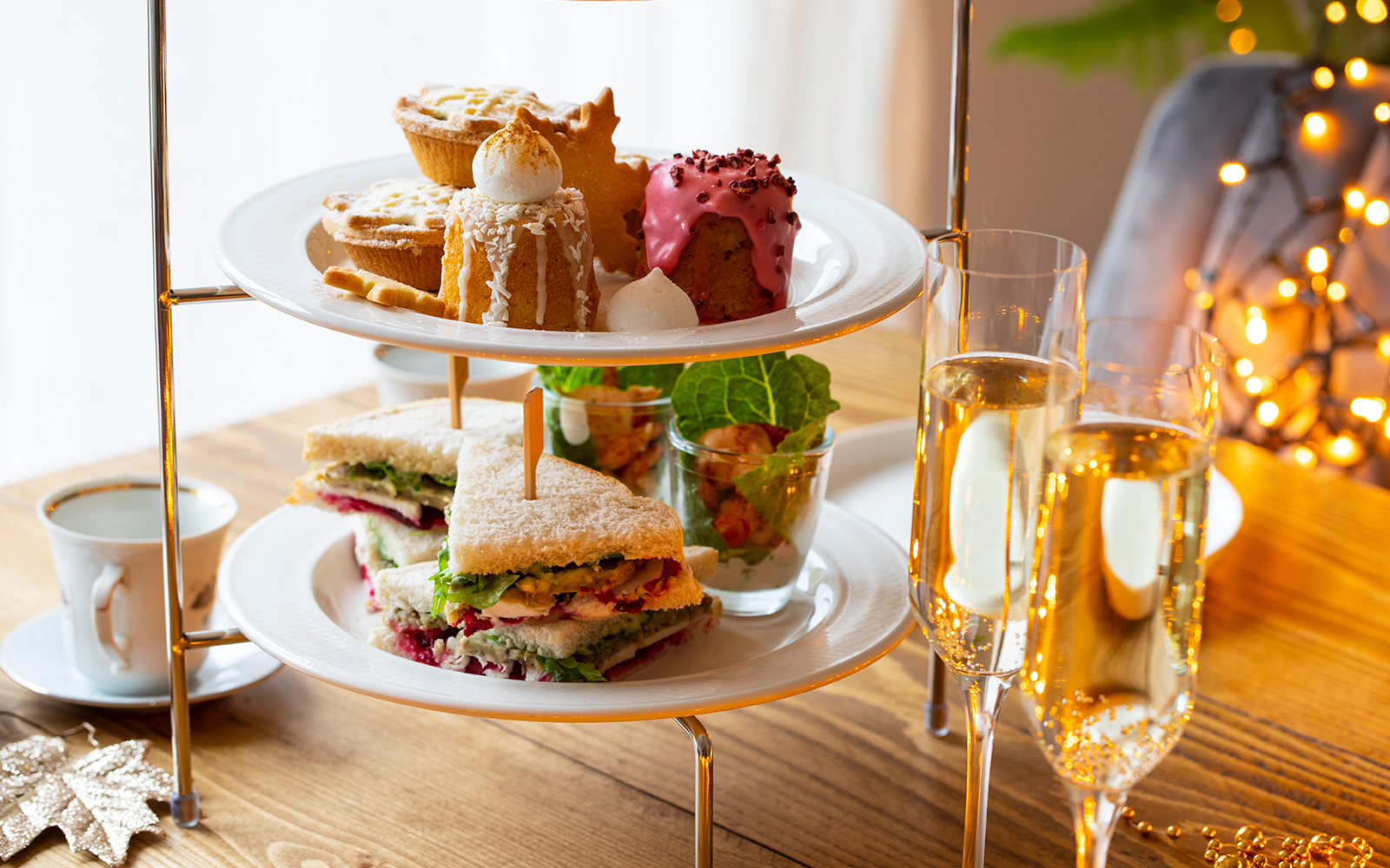 Traditional Christmas afternoon tea with sandwiches, pastries, and champagne on a wooden table.
