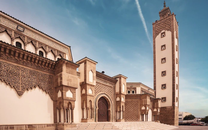 Agadir mosque with intricate architecture and tall minaret under a clear sky.
