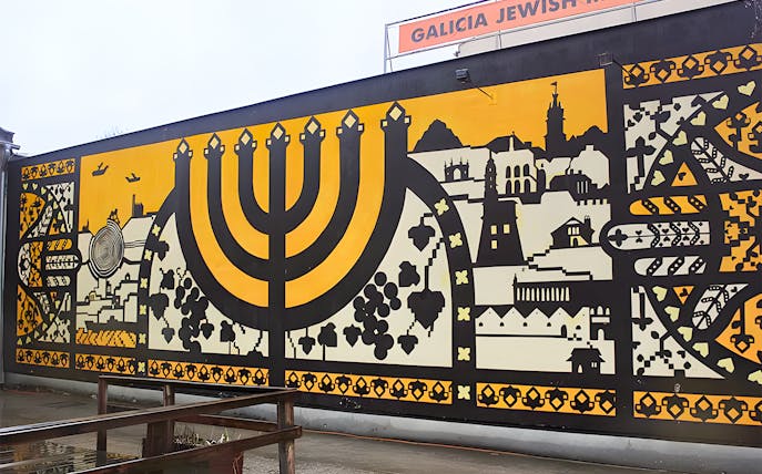 Mural at Galicia Jewish Museum in Kraków featuring a large menorah and cityscape.