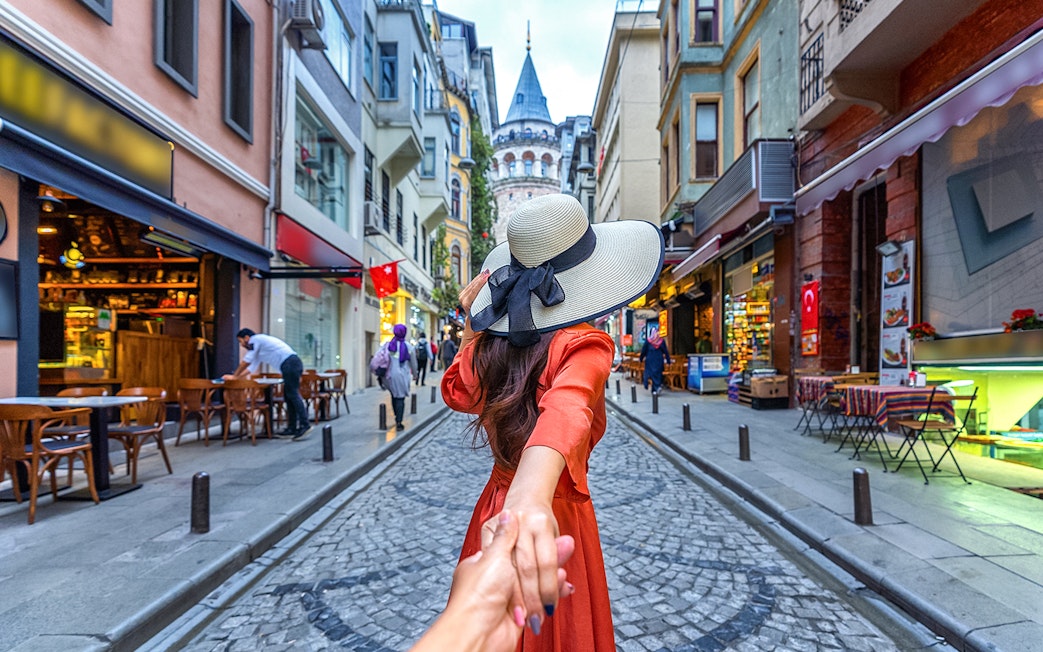 Couple holding hands on a cobblestone street with Galata Tower in Istanbul.