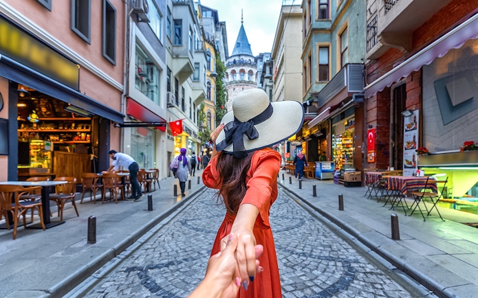 Couple holding hands on a cobblestone street with Galata Tower in Istanbul.