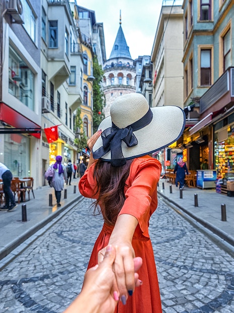 Couple holding hands on a cobblestone street with Galata Tower in Istanbul.
