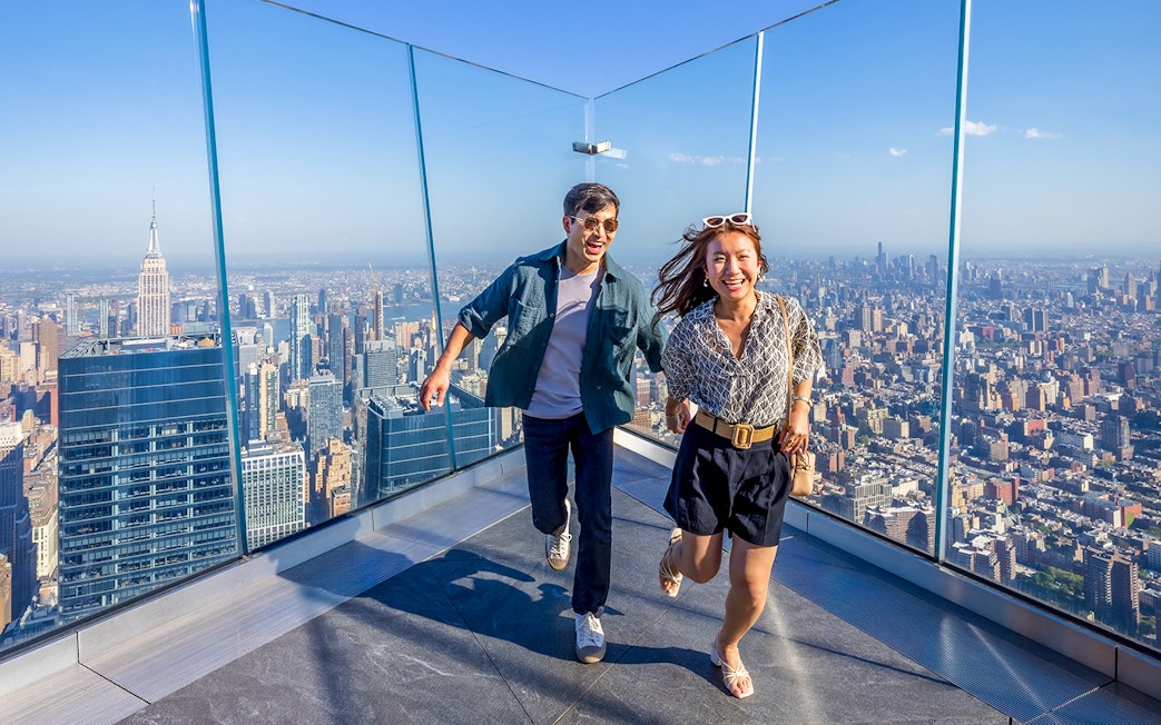 Visitors enjoying the view from an observation deck in New York City with the Empire State Building in the background.