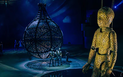 Performers in intricate costumes with a large spherical structure at La Perle show, Dubai.