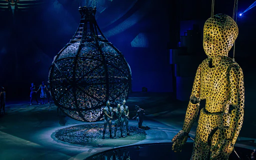 Performers in intricate costumes with a large spherical structure at La Perle show, Dubai.