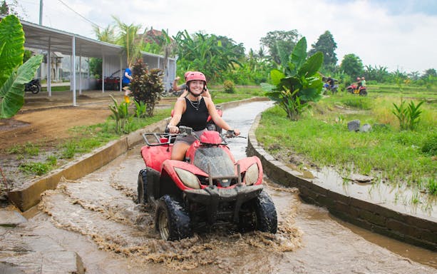 Person riding an ATV through a muddy path on a quad biking tour in a tropical setting.