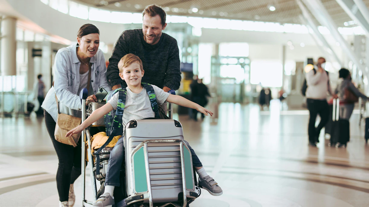 Parents pushing luggage trolley with son at airport terminal.