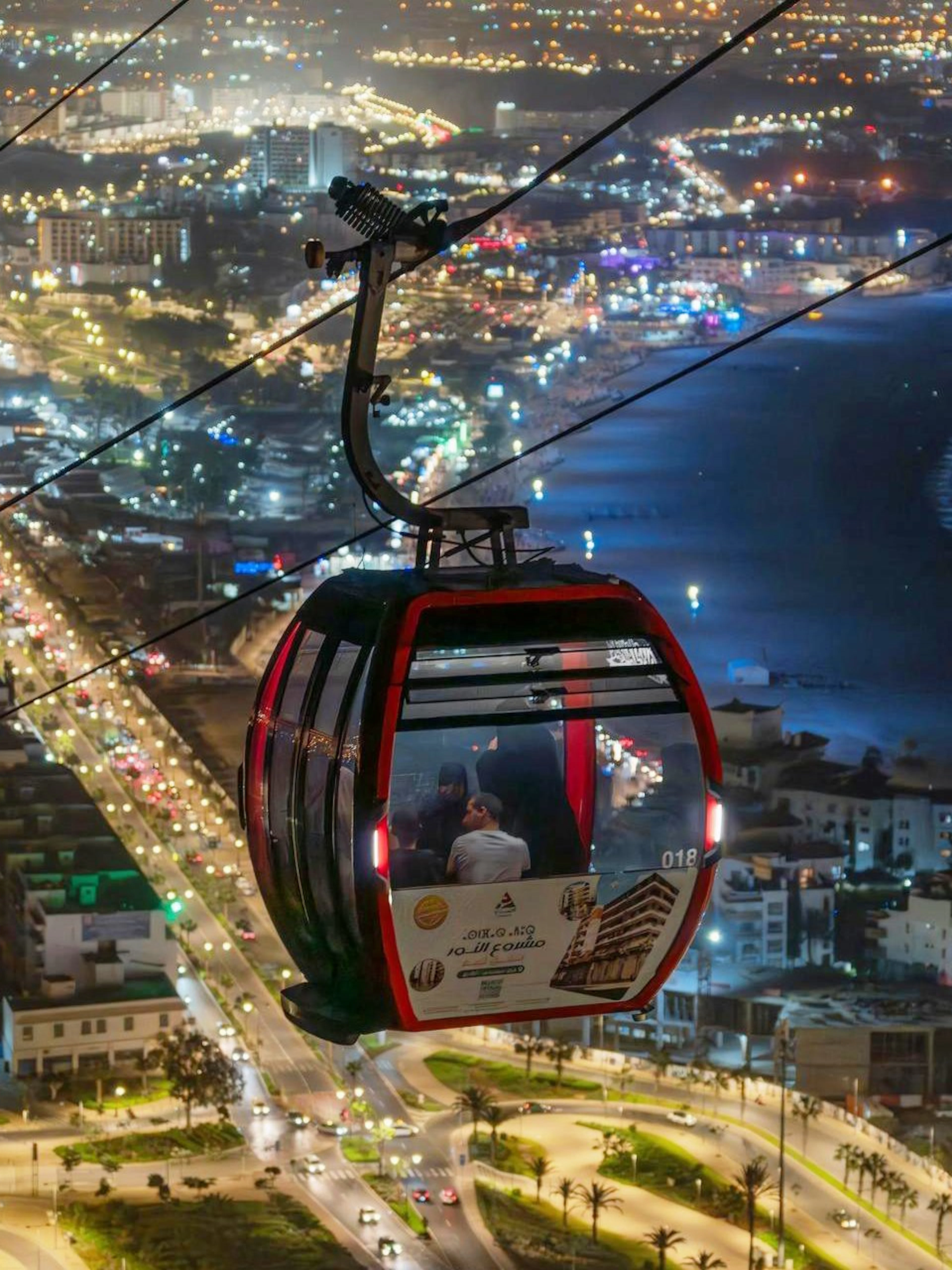 Nighttime view from a cable car over city lights and coastline.