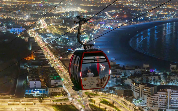 Nighttime view from a cable car over city lights and coastline.