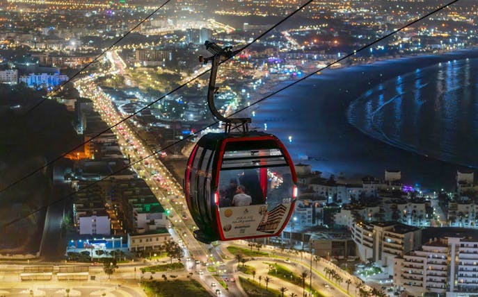 Nighttime view from a cable car over city lights and coastline.