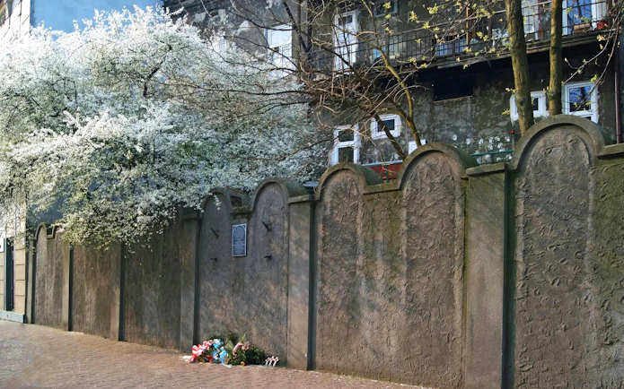 Ghetto wall fragment in Krakow with memorial flowers at the base.