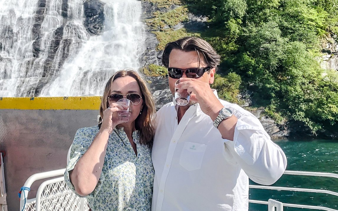 Couple enjoying drinks on a boat near the Bachelor Waterfall, Geiranger Fjord, Norway.