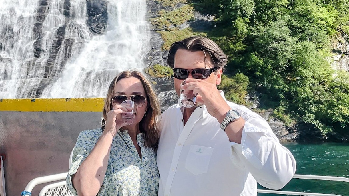 Couple enjoying drinks on a boat near the Bachelor Waterfall, Geiranger Fjord, Norway.