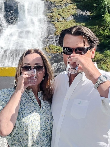 Couple enjoying drinks on a boat near the Bachelor Waterfall, Geiranger Fjord, Norway.