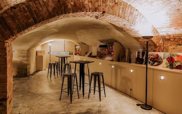Wine tasting room with Châteauneuf-du-Pape sign and bar stools in a brick cellar.