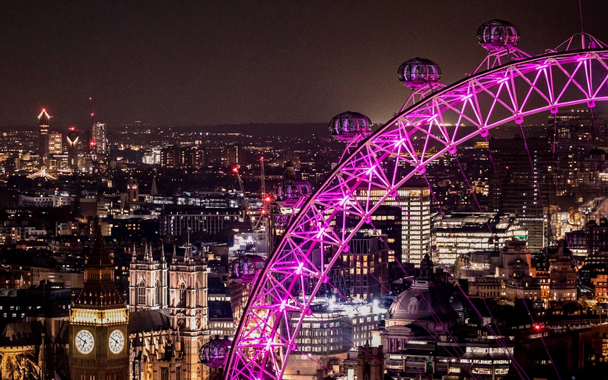 London Eye illuminated at night with city skyline in the background.