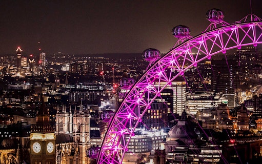 London Eye illuminated at night with city skyline in the background.