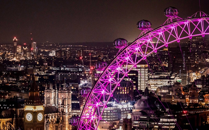 London Eye illuminated at night with city skyline in the background.