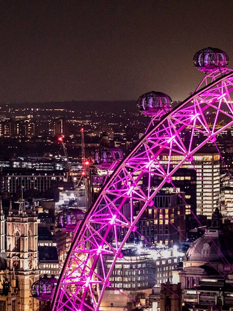 London Eye illuminated at night with city skyline in the background.