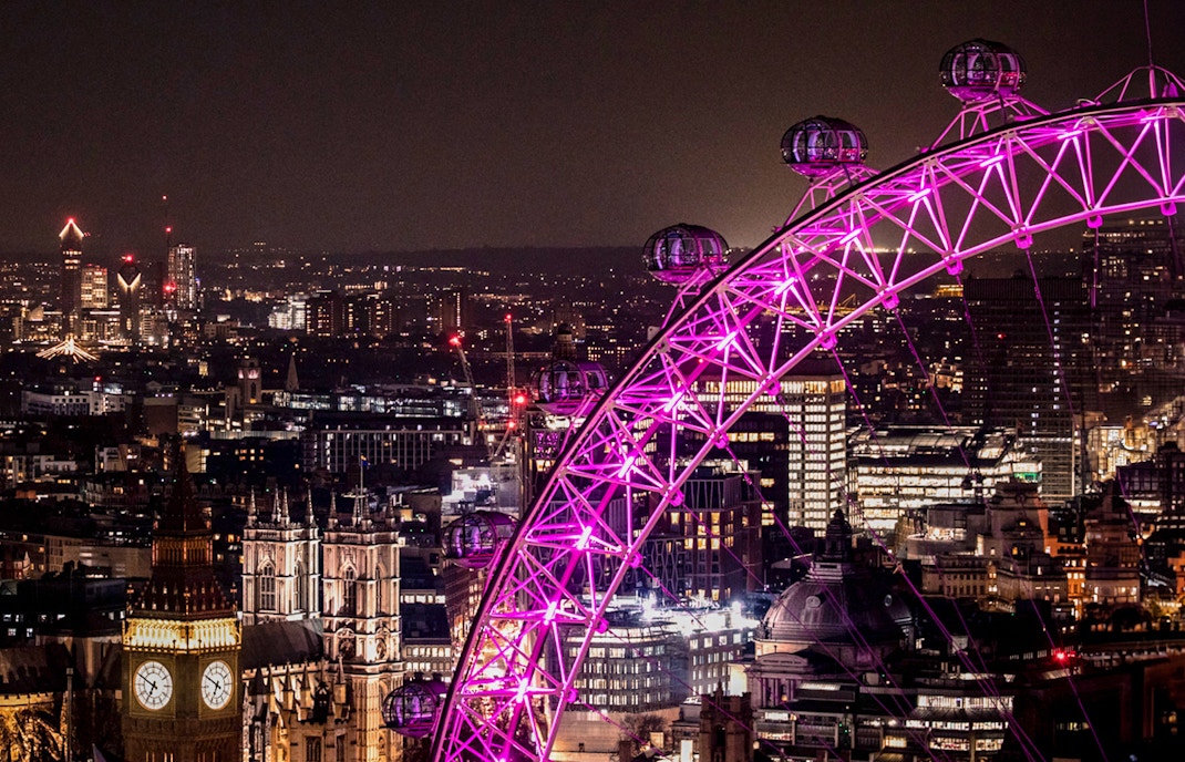 London Eye illuminated at night with city skyline in the background.