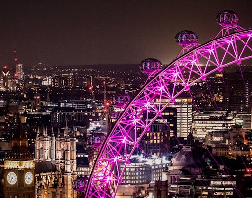 London Eye illuminated at night with city skyline in the background.