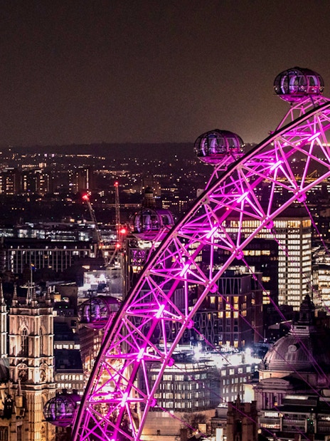 London Eye illuminated at night with city skyline in the background.