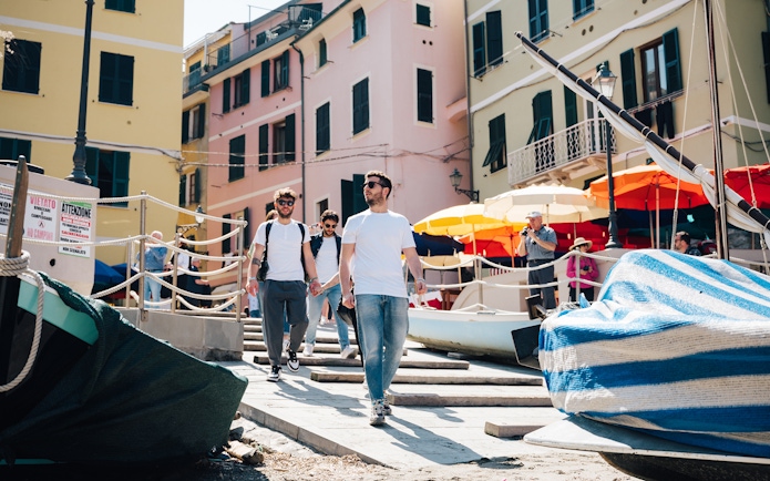 Tourists walking through colorful streets of Cinque Terre, Italy, with boats and umbrellas nearby.