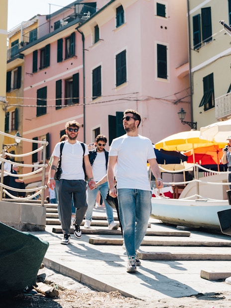 Tourists walking through colorful streets of Cinque Terre, Italy, with boats and umbrellas nearby.