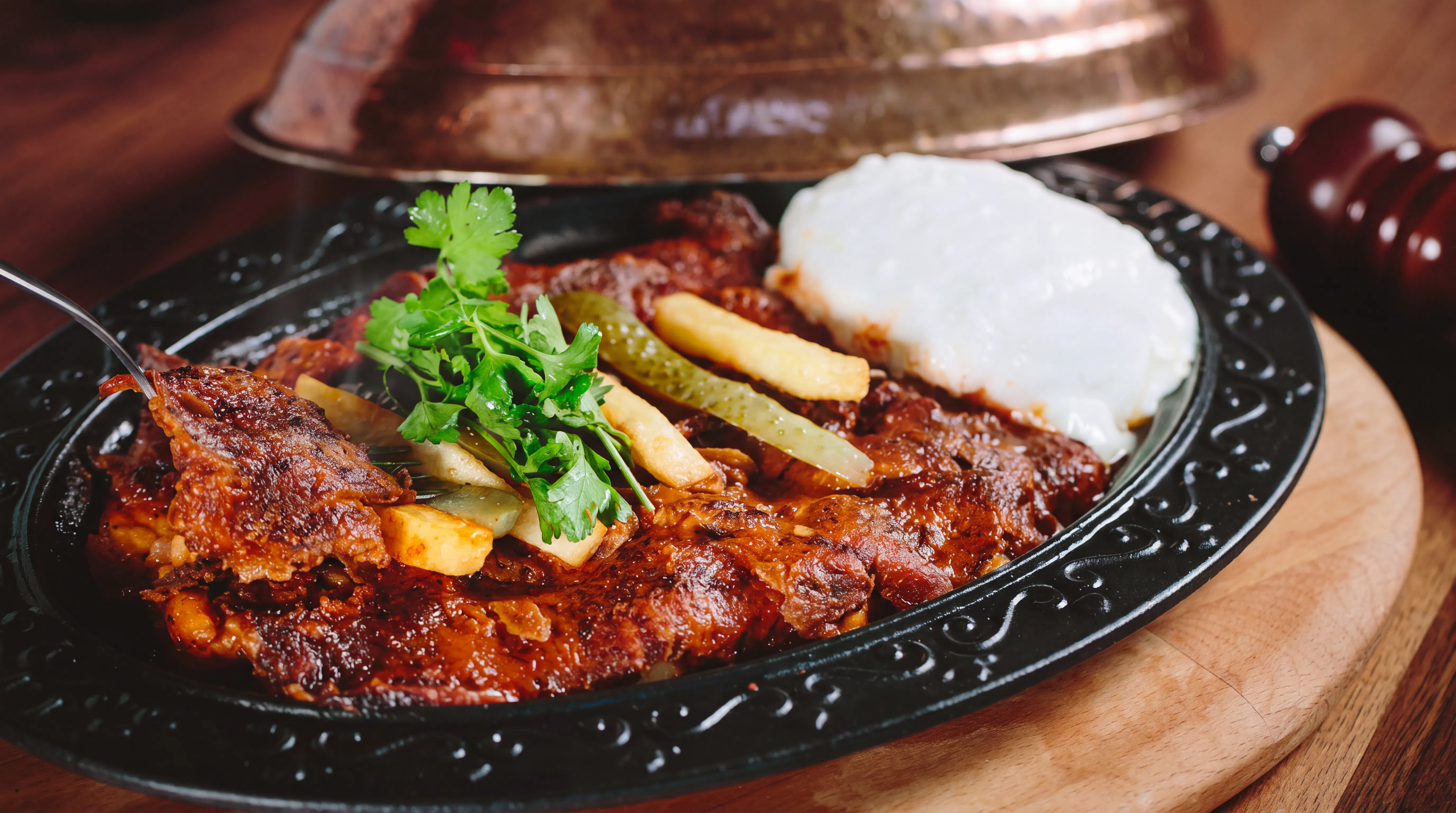 Turkish Iskender kebab with yogurt, fries, and herbs on a black plate.