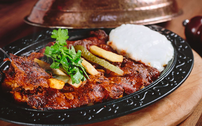 Turkish Iskender kebab with yogurt, fries, and herbs on a black plate.