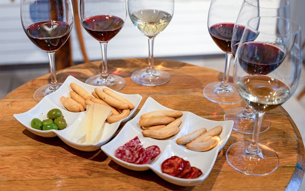 Wine tasting setup with red and white wines, cheese, olives, and cured meats on a wooden table.