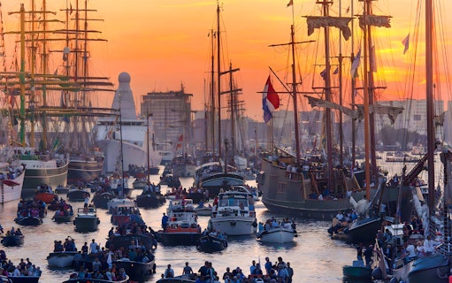 Tall ships and boats crowd the harbor during SAIL Amsterdam evening event.