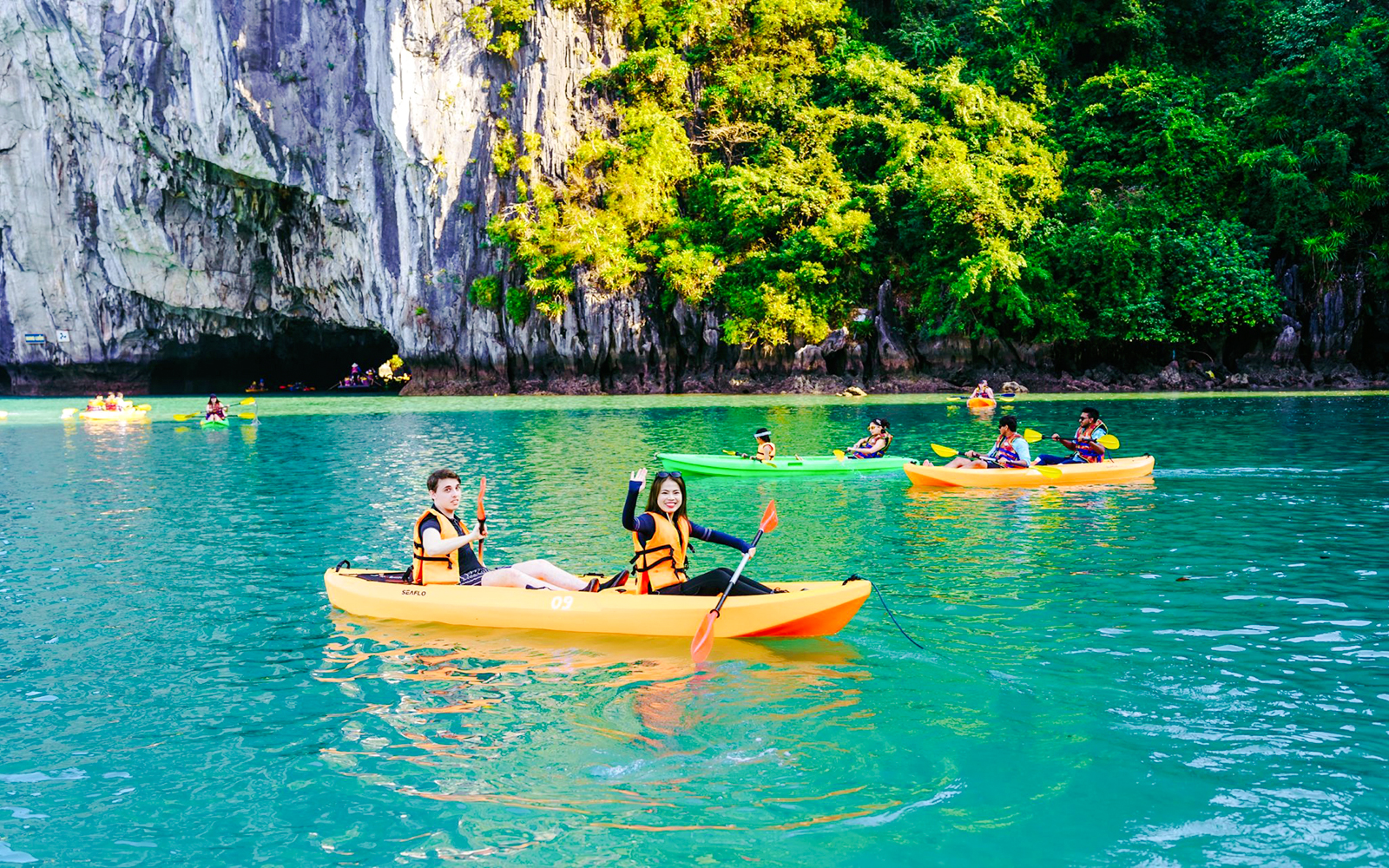 Tourists kayaking on turquoise waters in Ha Long Bay with karst formations in the background.