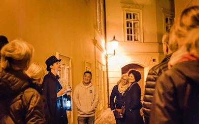 Tour guide with lantern leading Ghosts & Legends of Old Town Prague tour at night.