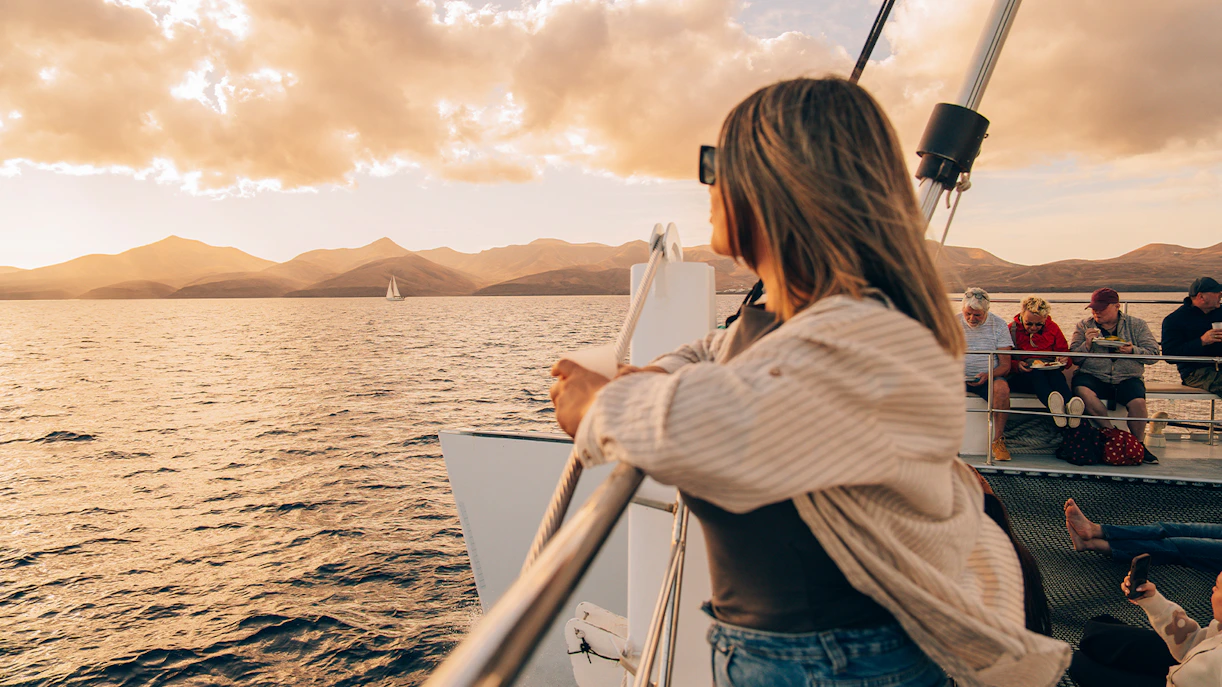 Tourist on boat enjoying Lanzarote sunset with distant sailboat.