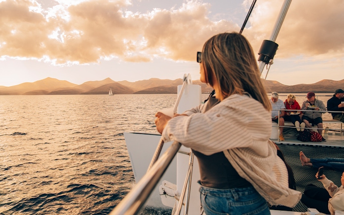 Tourist on boat enjoying Lanzarote sunset with distant sailboat.