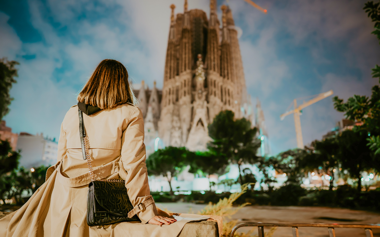 Woman viewing Sagrada Familia Basilica's illuminated facade at night in Barcelona.