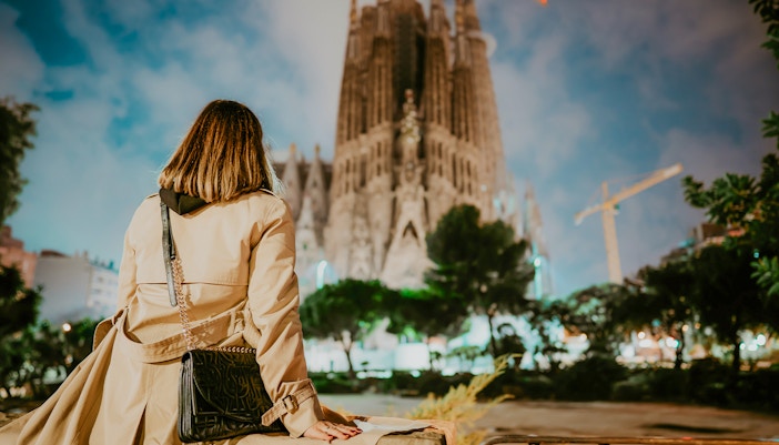 Woman viewing Sagrada Familia Basilica's illuminated facade at night in Barcelona.