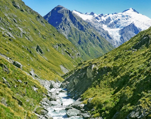 Trekker crossing a bridge over a stream between Rees and Dart River in Mt. Aspiring National Park, New Zealand.