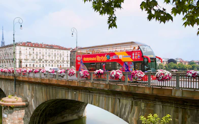 Turin hop-on hop-off bus crossing a bridge with cityscape in the background.
