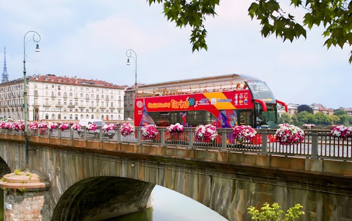 Turin hop-on hop-off bus crossing a bridge with cityscape in the background.
