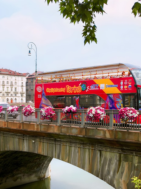 Turin hop-on hop-off bus crossing a bridge with cityscape in the background.
