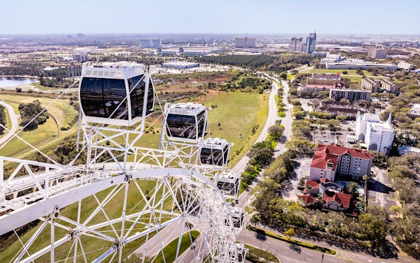 Ferris wheel cabins at ICON Park, Orlando with cityscape and greenery in the background.