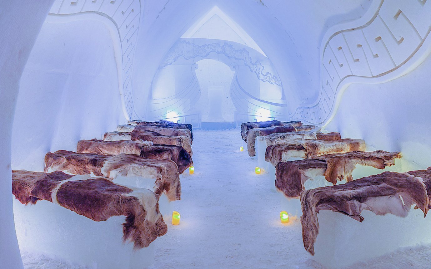Inside view of Arctic SnowHotel with ice benches covered in fur and ambient lighting.