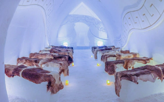 Inside view of Arctic SnowHotel with ice benches covered in fur and ambient lighting.