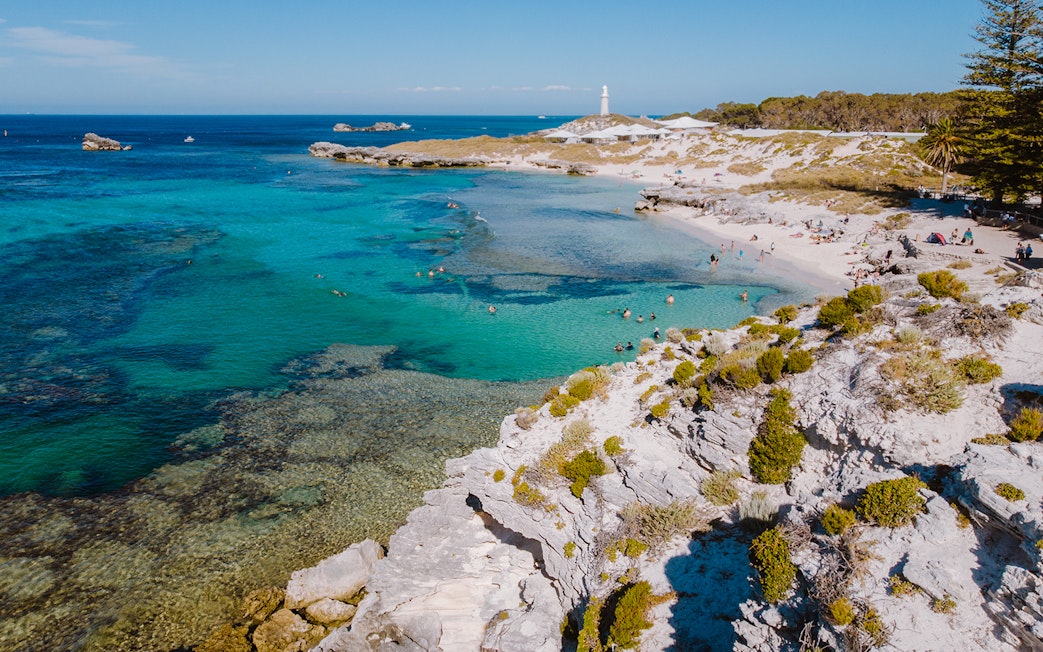 Tourists swimming at a beach on Rottnest Island with a lighthouse in the distance.