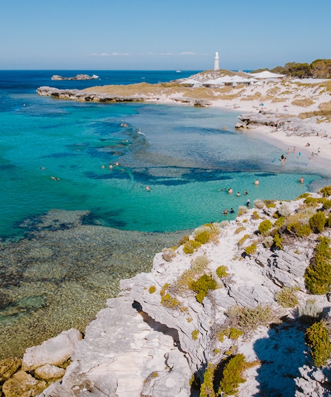 Tourists swimming at a beach on Rottnest Island with a lighthouse in the distance.